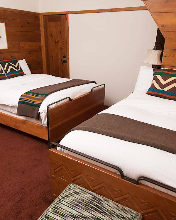 A Timberline queen + double room pictured with a Pendleton blankets draped over the beds and wood-paneled walls.