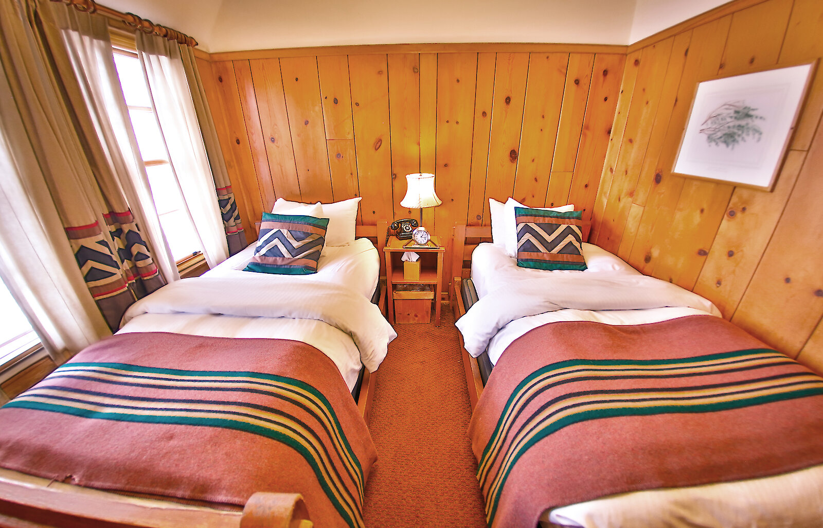 A Economy Twin room pictured with a Pendleton blankets draped over the beds and wood-paneled walls.