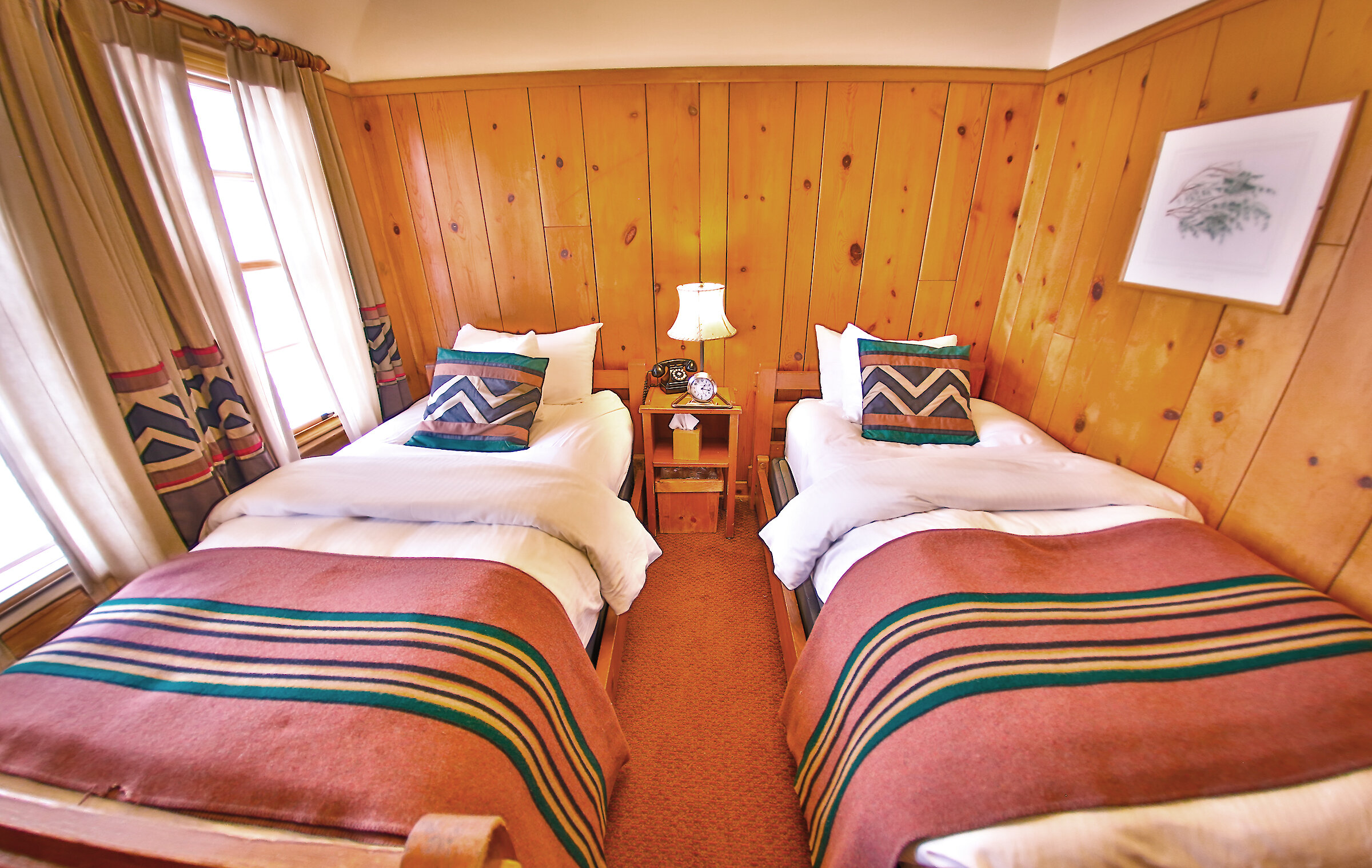 A Economy Twin room pictured with a Pendleton blankets draped over the beds and wood-paneled walls.