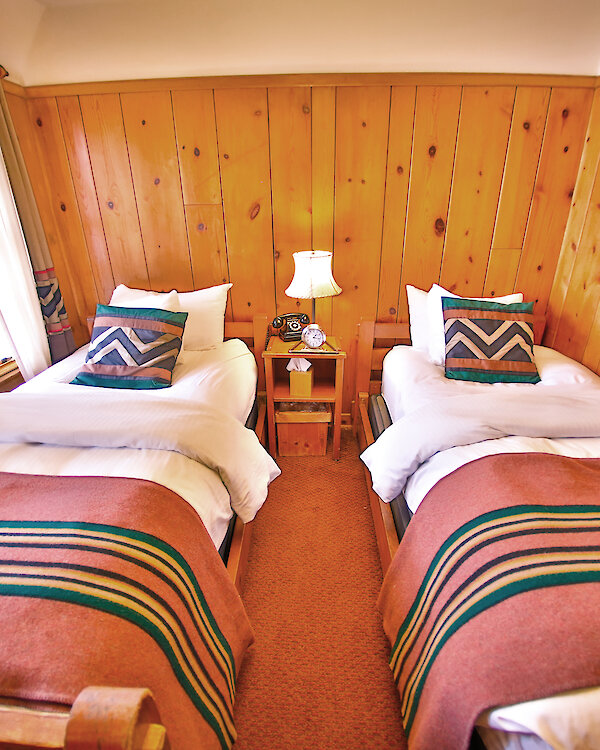 A Economy Twin room pictured with a Pendleton blankets draped over the beds and wood-paneled walls.